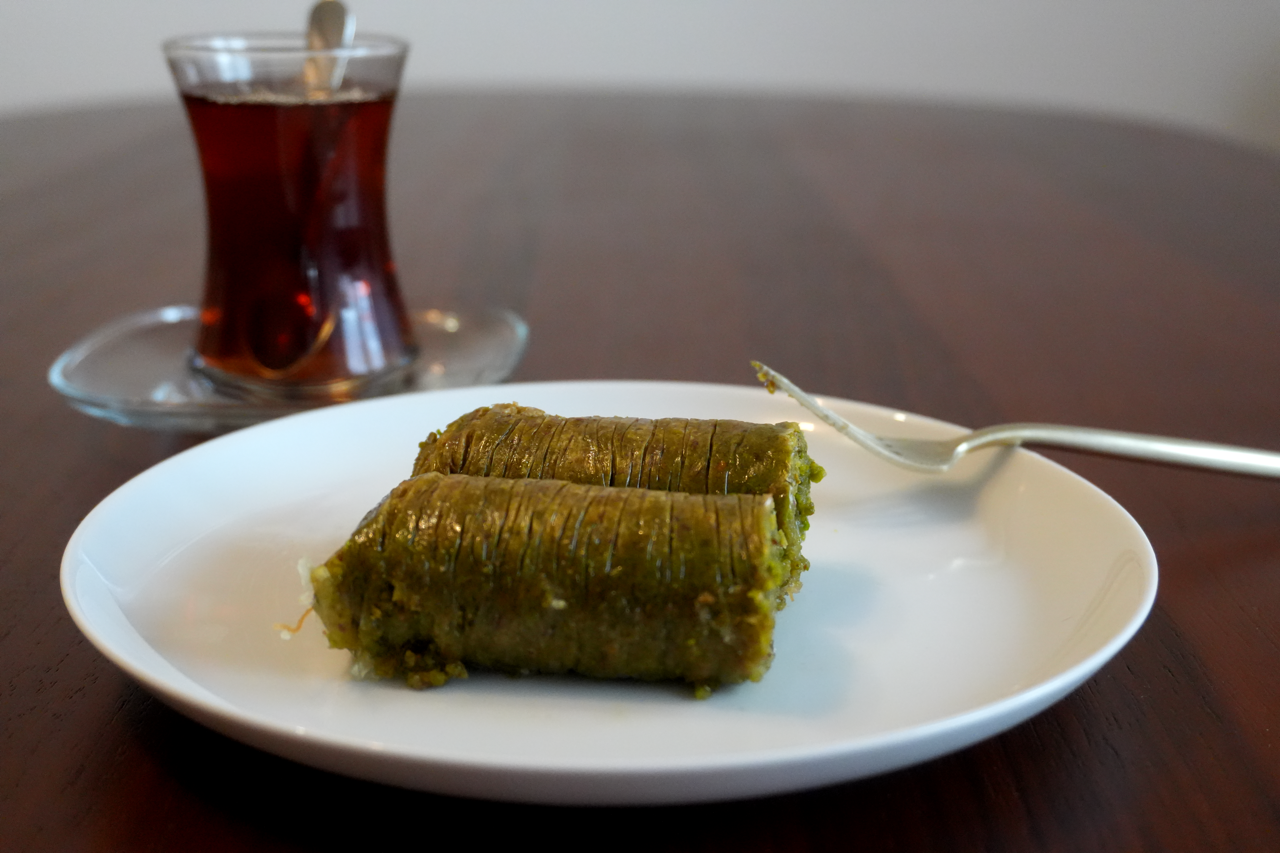 Sarma Baklava mit Pistazie: zart gerollte Pistazien-Baklava auf Teller, Tee im Hintergrund.