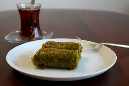 Sarma Baklava mit Pistazie: zart gerollte Pistazien-Baklava auf Teller, Tee im Hintergrund.