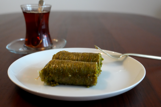 Sarma Baklava mit Pistazie: zart gerollte Pistazien-Baklava auf Teller, Tee im Hintergrund.